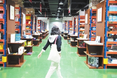5月5日，在賀蘭縣德勝工業園區的新華書店德勝倉賣場，一位市民在書架間穿梭。該賣場由占地面積1600平方米的書店倉庫轉型而來，人們可以推著購物車，像在超市一樣穿梭在書架間選購圖書。賣場書籍總量超過10萬冊，還著重營造閱讀環境，設置了閱讀區、文創區等區域。    本報記者  季正  攝